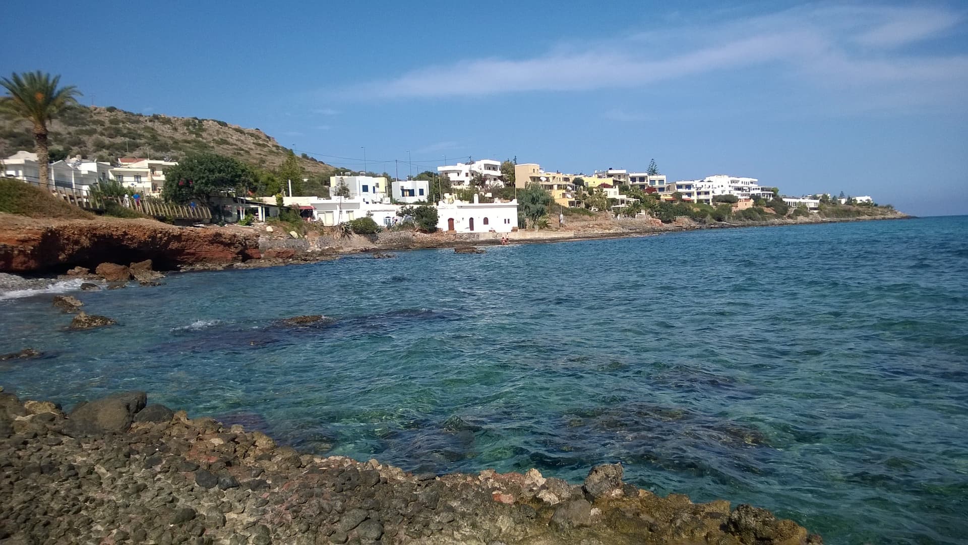 De rotsige kust bij Stalis op Kreta met palmen, witte vakantiehuizen en helderblauw water onder een zomerse lucht