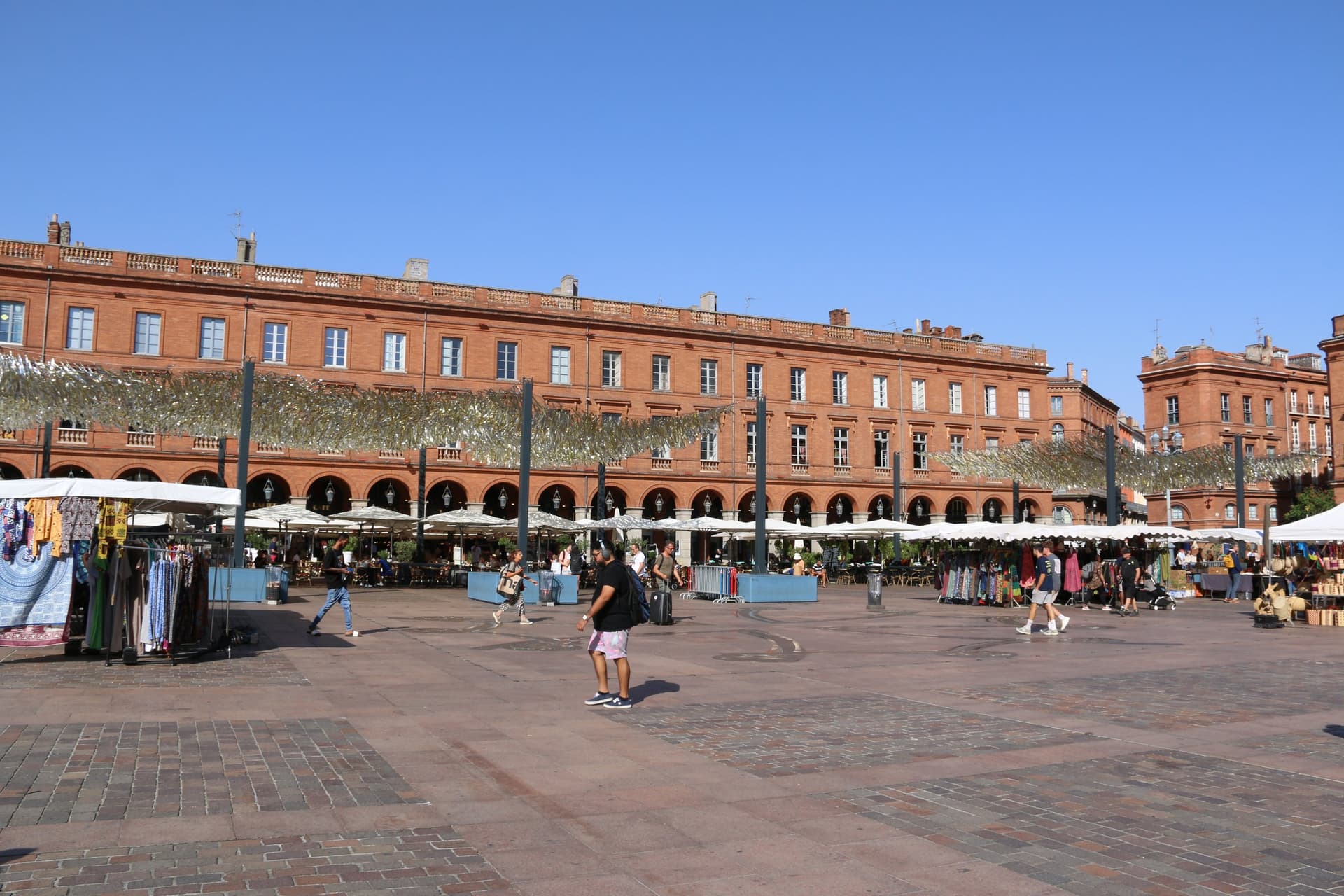 Het roodbakstenen Capitole aan de zonnige Place du Capitole in Toulouse, met marktkramen op het plein