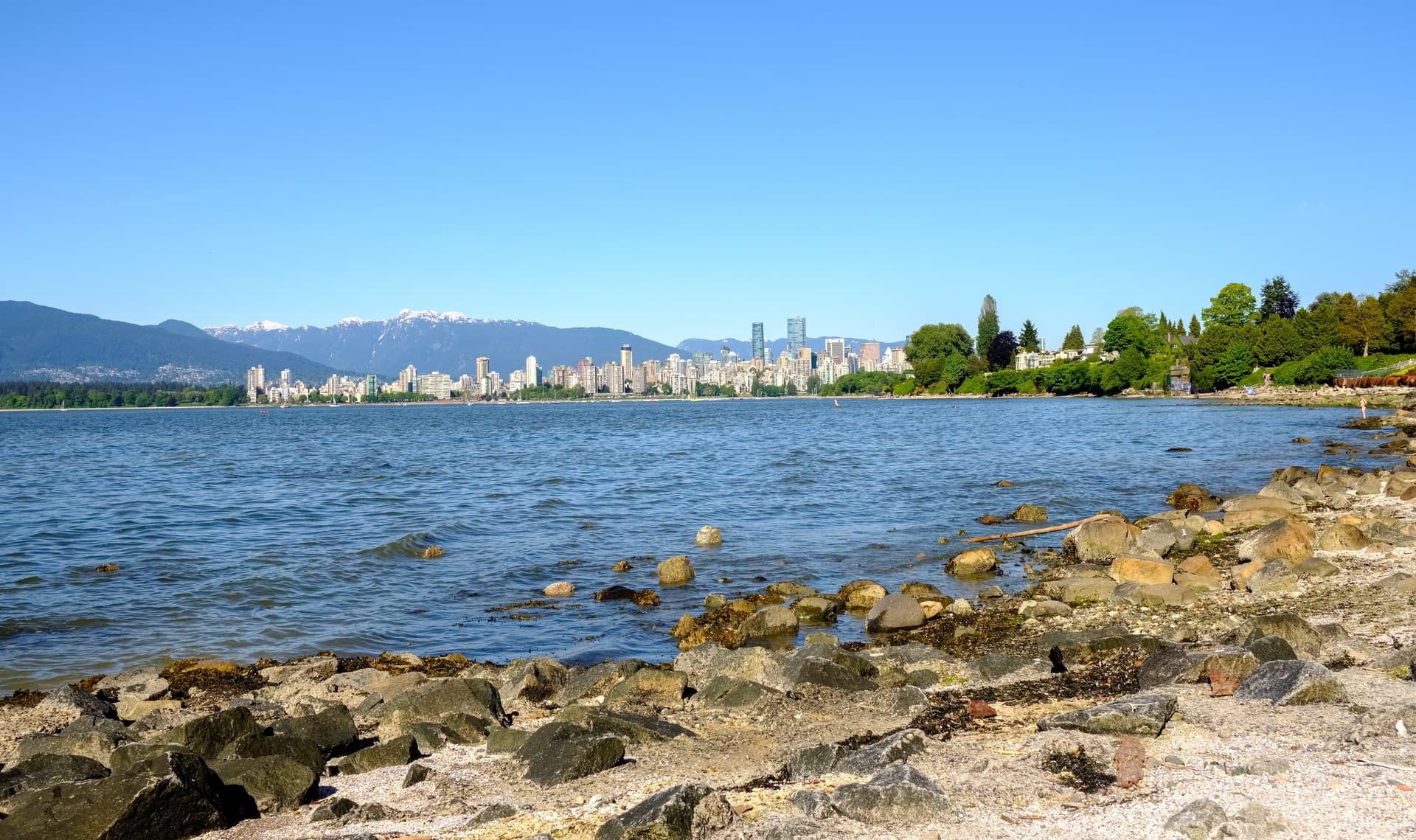 De skyline van downtown Vancouver gezien over het water onder een strakblauwe lucht, met besneeuwde bergtoppen erachter