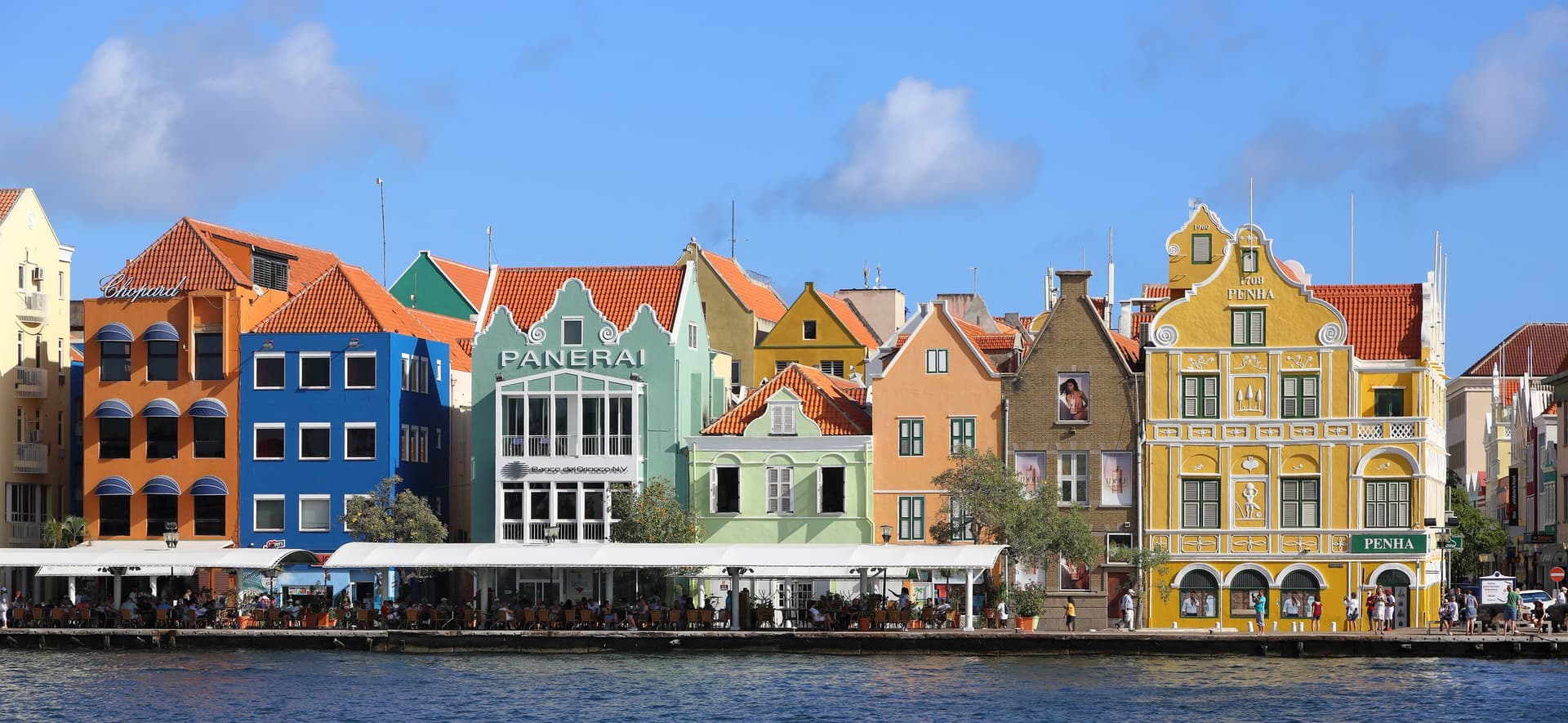 De pastelkleurige koopmanshuizen met trapgevels langs de Handelskade in Punda, Willemstad, gezien over het water van de Sint Annabaai